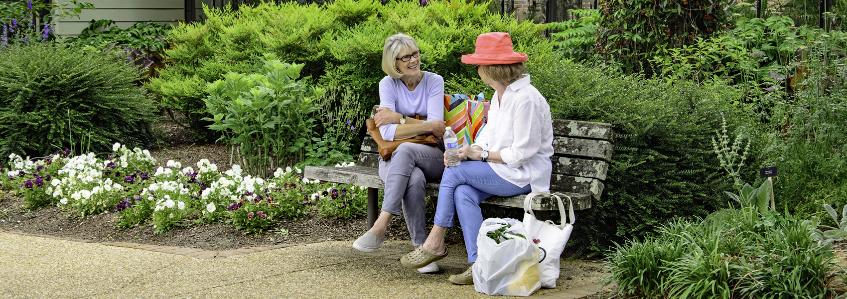 Two people rest on a bench alongside a garden