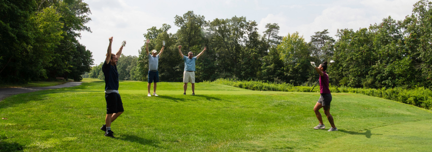 four golfers standing on the green with their arms in the air in celebration, participating in the Duffer's Tournament