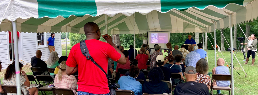 a bunch of people gathered under a tent listening to a speaker on Juneteenth