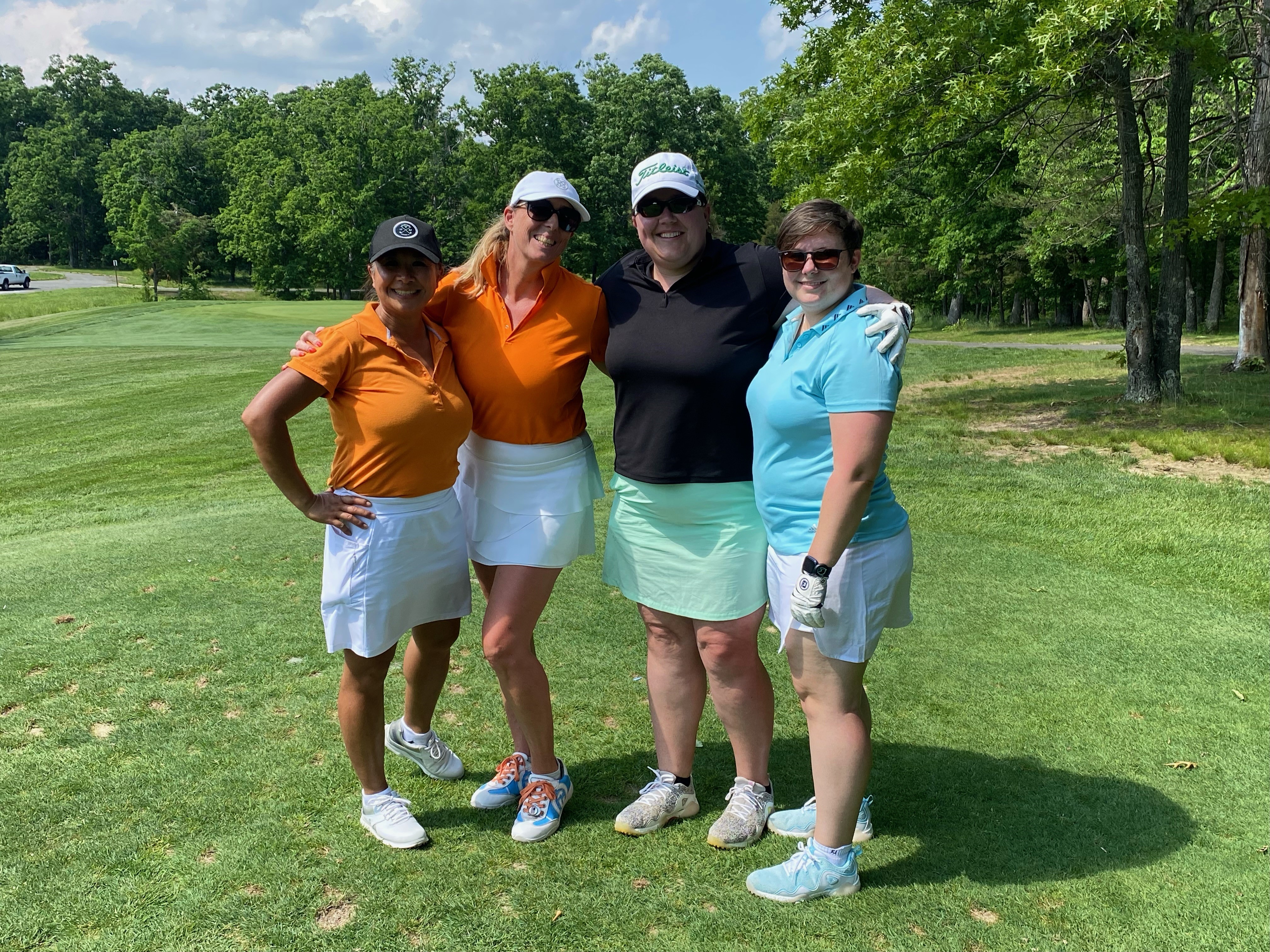 four women in golf outfits standing on the green with their arms around each other during Women's Golf Month