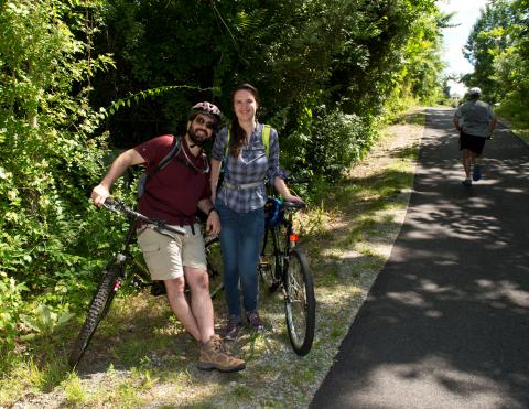 two bicyclists enjoying a paved trail surrounded by lush green trees