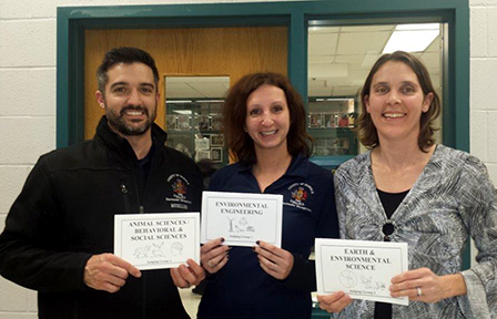 Three public works employees hold cards displaying the science fair categories they judged