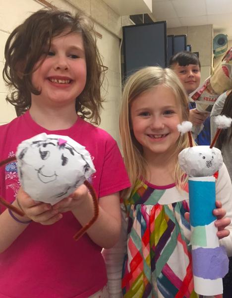 Two smiling girls hold caddisfly craft projects