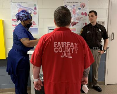 Nurse prepares to give inmate a dose of medication while deputy watches.