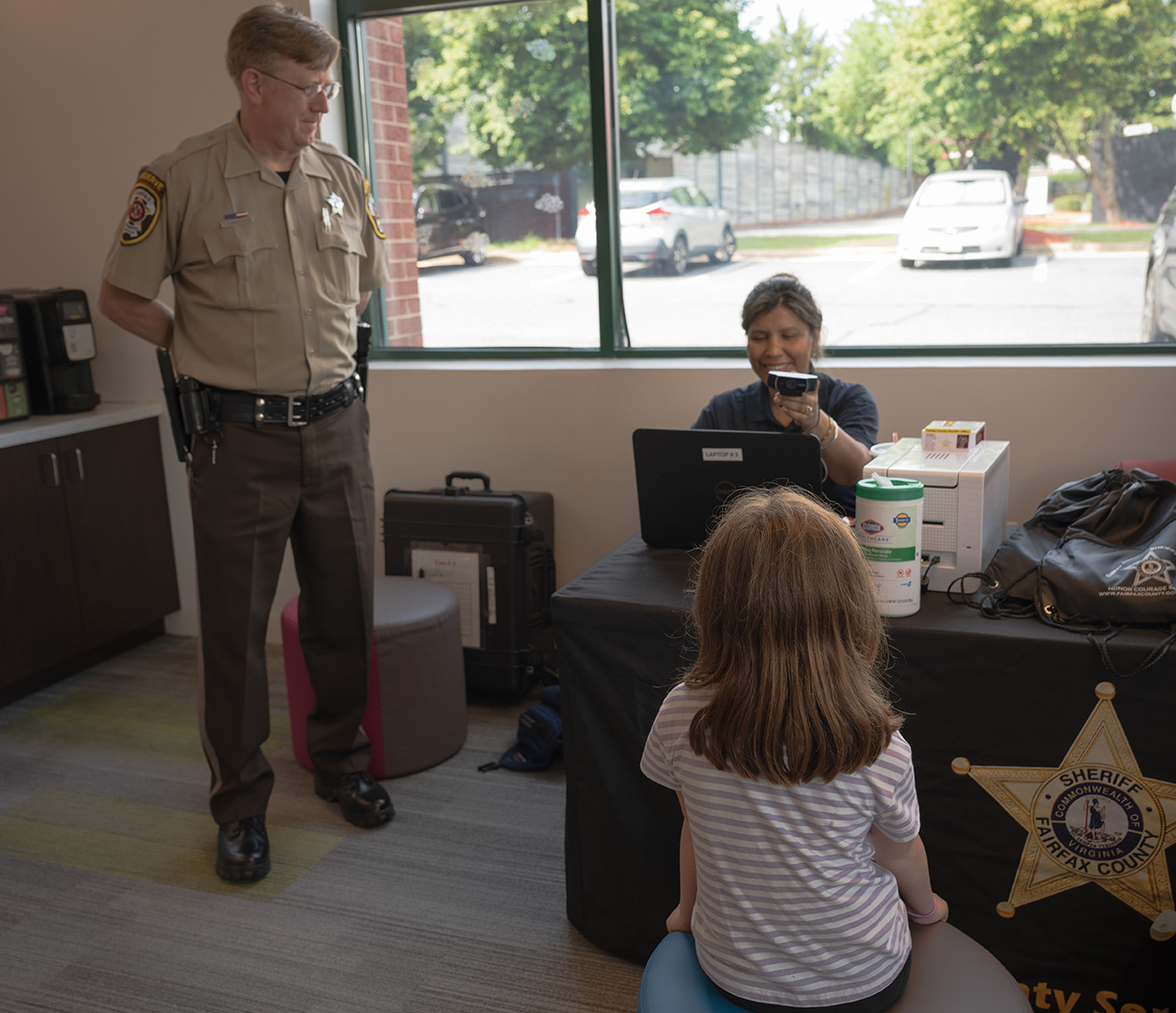 A reserve deputy sheriff looks on as a child has her photo taken for her identification card. 