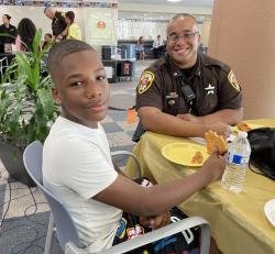 Deputy sheriff and young man enjoy pizza.