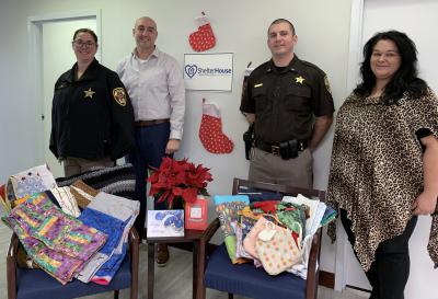 Two deputies and two Shelter House representatives with quilts