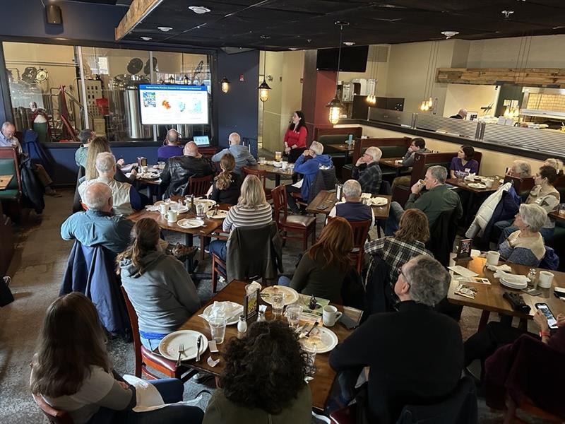 A group of people listen to a speaker at a restaurant.